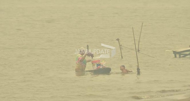 Seorang ibu terlihat menjalankan aktivitas di Sungai Batanghari di tengah kabut asap.