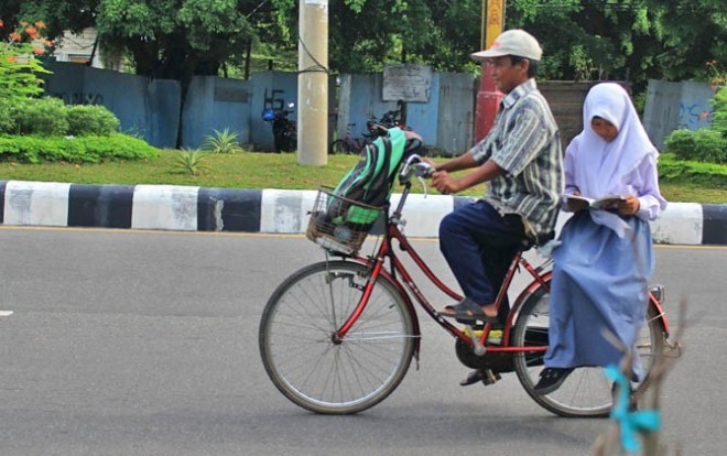Dewi Mulyani dibonceng ayahnya Mardani dengan sepeda angin sambil membaca buku saat melintas di Jalan P Diponegoro, Palangka Raya, Kalteng, Rabu (1/3). Foto tersebut menjadi perbincangan hangat di media sosial (medsos). (Agus Pramono/Kalteng Pos)