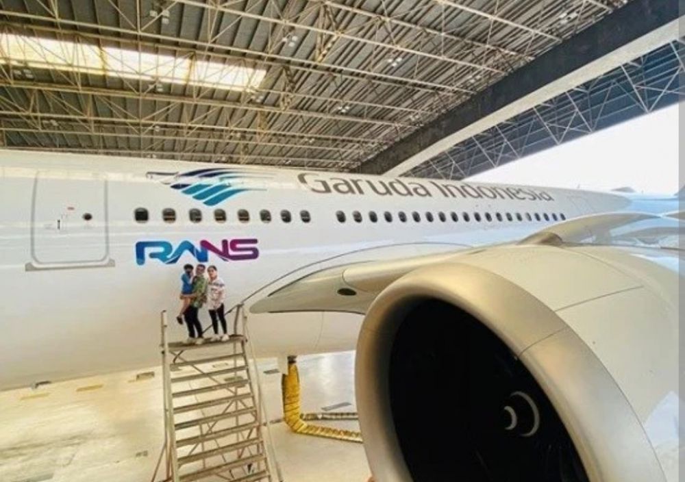 Raffi Ahmad, Nagita Slavina serta putranya, Rafathar Malik Ahmad berdiri di samping bodi pesawat Garuda Indonesia dengan logo RANS perusahaan Raffi. 