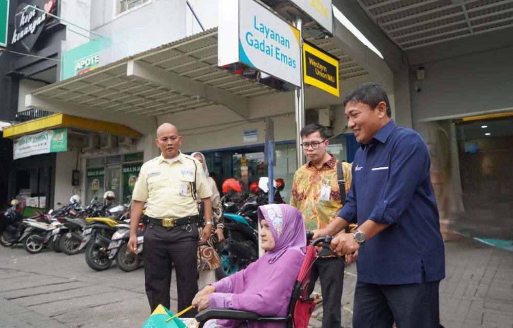 Wakil Direktur Utama BSI Bob Tyasika Ananta (kanan) membantu mendorong kursi roda saat mengantarkan salah seorang nasabah BSI pada kunjungannya di BSI KCP Gresik Kota Baru, Senin (4/12).